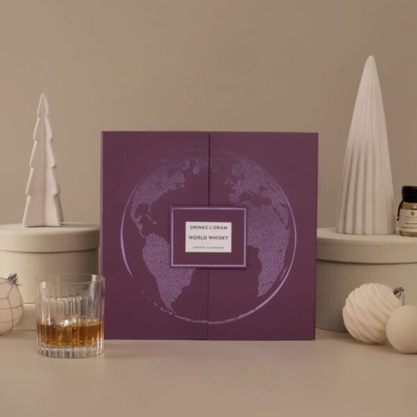 World whisky advent calendar in a purple gift box with a globe design, beside a whisky tumbler, a sample bottle, white ceramic trees and baubles
