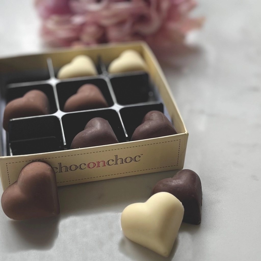 A box of assorted heart-shaped chocolates featuring milk, white, and dark chocolate hearts on a marble surface.