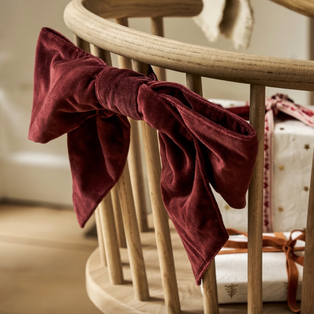 A plush berry red cotton velvet Christmas door bow tied elegantly to the wooden spindles of a chair.
