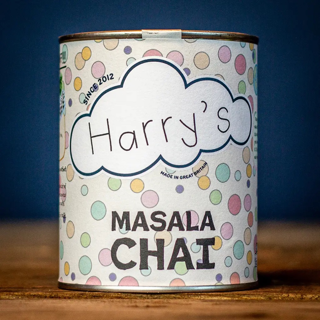 Recyclable polka-dot tin of Harry's Masala Chai tea handcrafted in Great Britain, resting on a rustic wooden table.