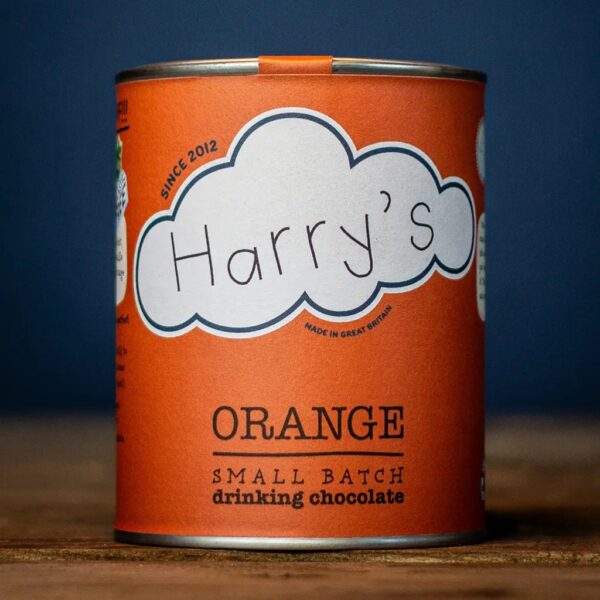 Recyclable vibrant orange tin of Harry's Small Batch Orange Drinking Chocolate resting on a rustic wooden surface.