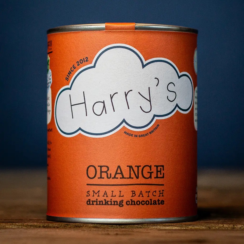 Recyclable vibrant orange tin of Harry's Small Batch Orange Drinking Chocolate resting on a rustic wooden surface.