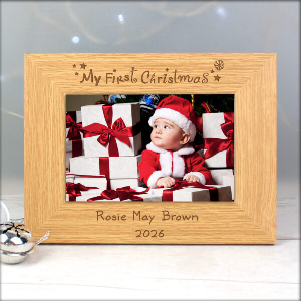 An oak veneer landscape photo frame engraved with 'My First Christmas' at the top and 'Rosie May Brown 2026' at the bottom, holding a picture of a baby in a Santa suit surrounded by gifts.