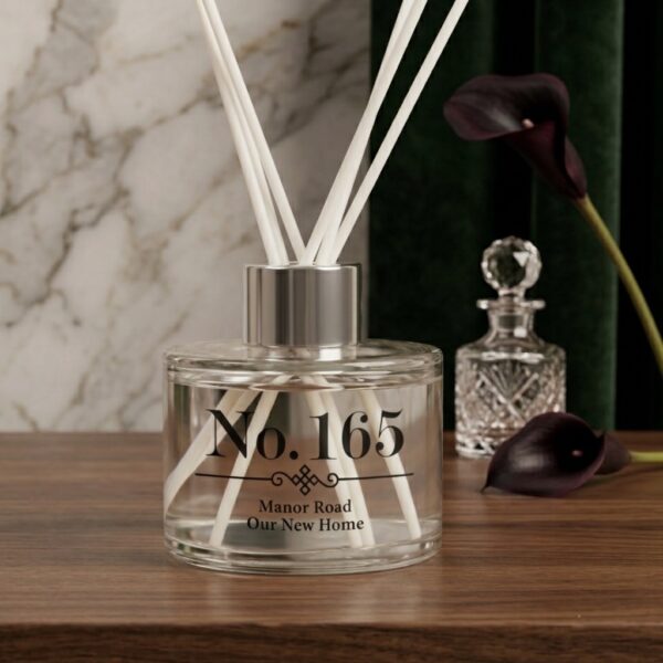 Personalised glass reed diffuser with silver collar on a dark wood surface set against marble and deep green velvet background by Abode Home & Gifts