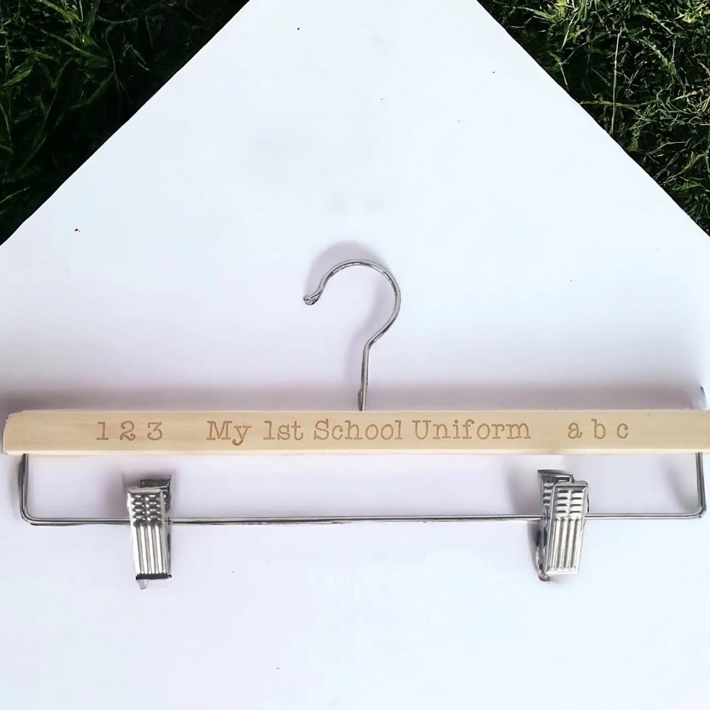 Laser-engraved wooden uniform clip hanger reading "1 2 3 My 1st School Uniform a b c" on a white background with grass border.