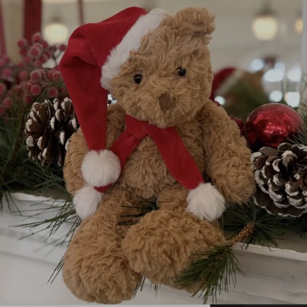 Cuddly Santa Bear plush teddy wearing a red hat and scarf sitting on a decorated festive mantelpiece.
