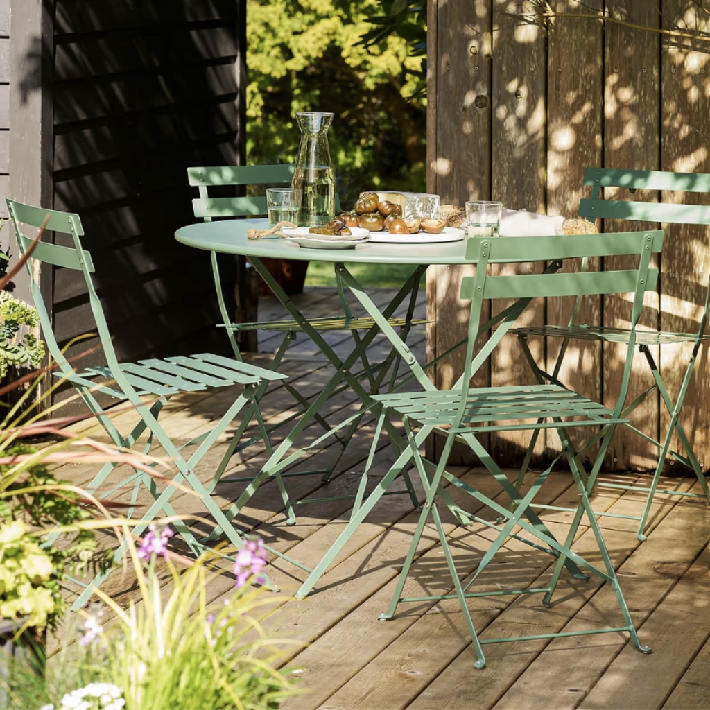Four-seater thistle green metal folding bistro table and chairs set styled with a carafe and platter on a wooden garden deck.