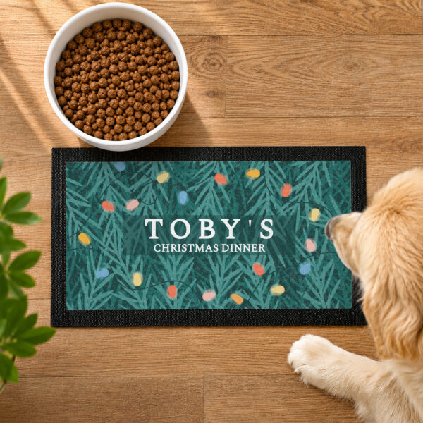 Overhead view of a personalised Christmas pet bowl mat with a retro fairy light pattern and text reading TOBY'S CHRISTMAS DINNER.