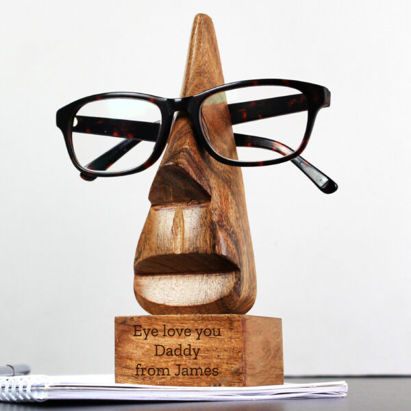 Personalised nose-shaped acacia wood glasses holder resting on a desk with tortoiseshell spectacles resting on the bridge.