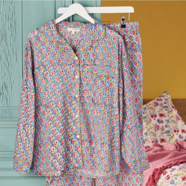 Blue and pink floral block print cotton pyjamas with green piping hanging against a painted blue door