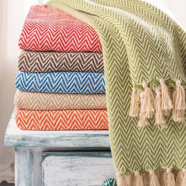 Folded chevron recycled cotton throws in red and orange stacked on a painted table with a tasselled throw draped over the side