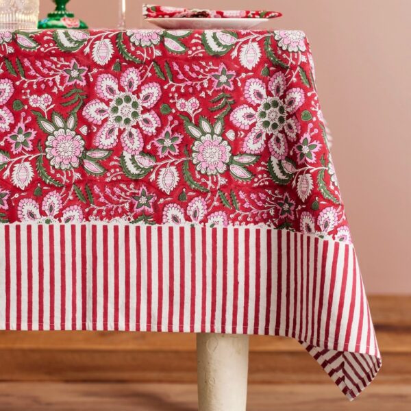 Red floral block print Christmas tablecloth with pink flowers and a red and white striped border on a dining table