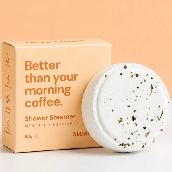 White menthol and eucalyptus shower steamer flecked with dried mint, beside its pastel peach gift box reading Better than your morning coffee