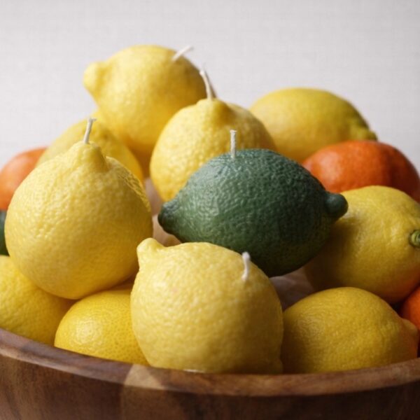 Realistic handmade lemon, lime and orange fruit candles with white wicks, piled in a wooden fruit bowl