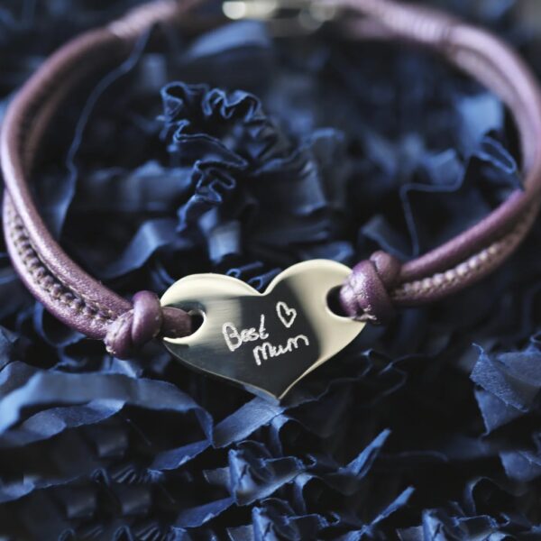 Berry double-strand leather bracelet with a polished stainless steel heart engraved in handwriting with Best Mum and a small heart, resting on blue zig-zag shred