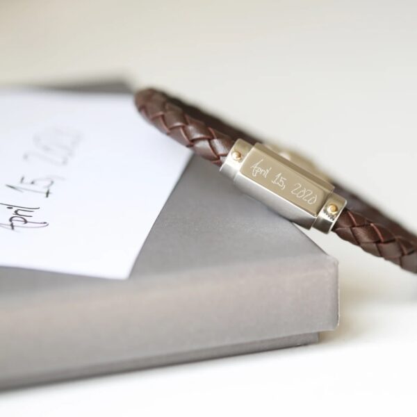 Brown braided leather bracelet with a stainless steel clasp engraved in handwriting with April 15, 2020, beside the original handwritten note on a grey gift box