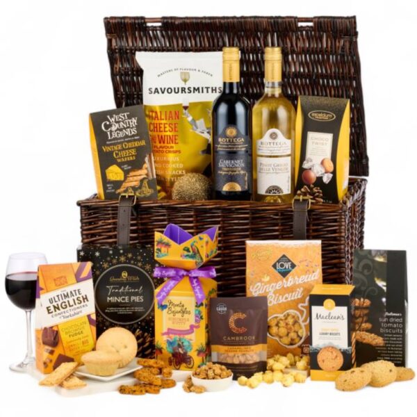 Christmas hamper with red and white wine, mince pies, fudge, popcorn, crisps and biscuits arranged around a dark wicker basket