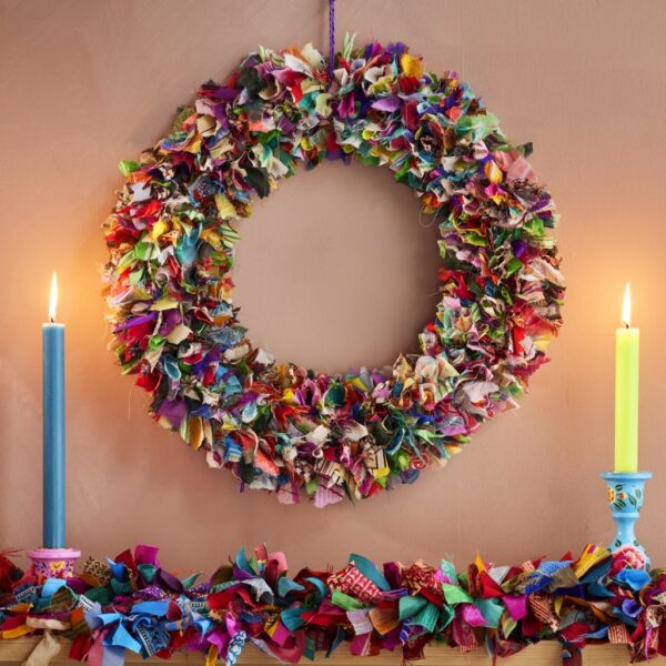 Large multicolour recycled sari wreath hanging above a mantelpiece with a matching sari garland and coloured candles
