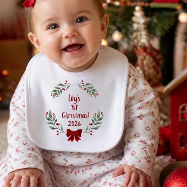 Smiling baby wearing a personalised first Christmas bib with a holly wreath, red bow and the name Lily