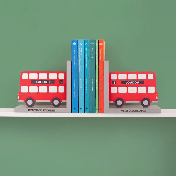 Personalised wooden London bus bookends holding children's books on a white shelf against a green wall