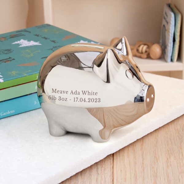 Personalised silver-plated piggy bank engraved with a baby name and birth details, displayed on a nursery table