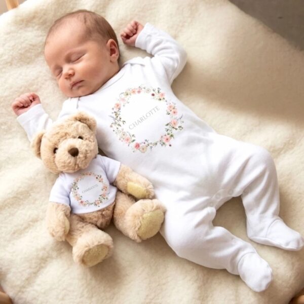Sleeping newborn in a personalised white vest with Charlotte wild flower wreath design, lying next to a matching teddy bear