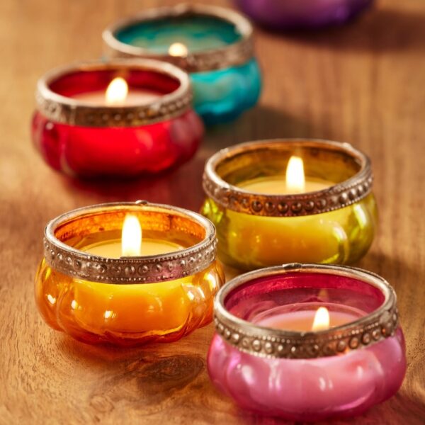 Six lit recycled glass pumpkin tealight holders with embossed iron borders in amber, pink, lime, red, turquoise and purple on a wooden table